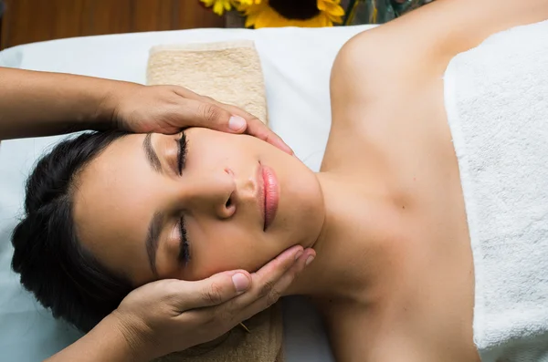 Modelo morena hispana recibiendo tratamiento de spa de masaje, manos trabajando en el masaje de la cabeza y la cara de las mujeres con los ojos cerrados — Foto de Stock