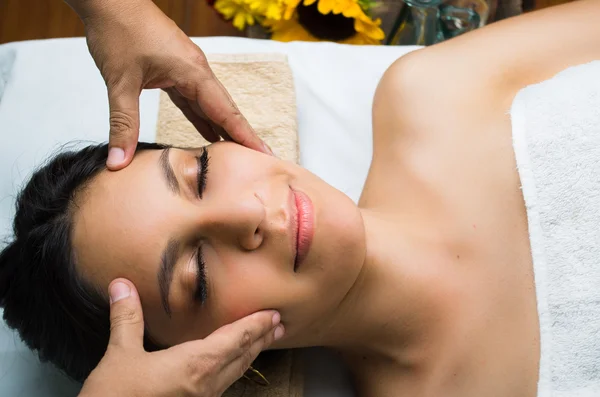 Modelo morena hispana recibiendo tratamiento de spa de masaje, manos trabajando en el masaje de la cabeza y la cara de las mujeres con los ojos cerrados — Foto de Stock