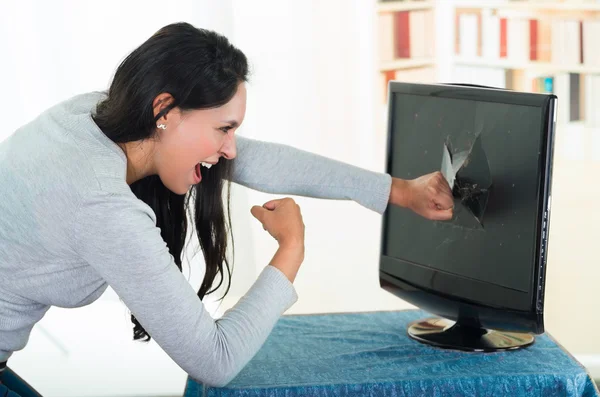 Arrabbiato femmina bruna punzonatura schermo del computer con grande foro su di esso — Foto Stock