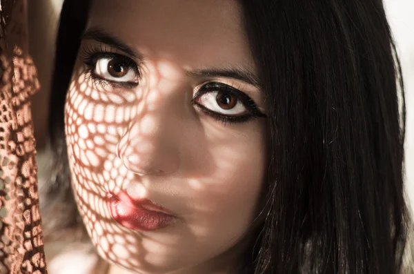Headshot brunette model using patterned shadows as artistic effect on face while posing — ストック写真
