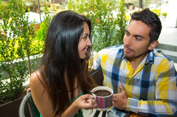 Hispanic cute couple enjoying coffee during a cozy date outdoors and green vegetation background — 图库照片