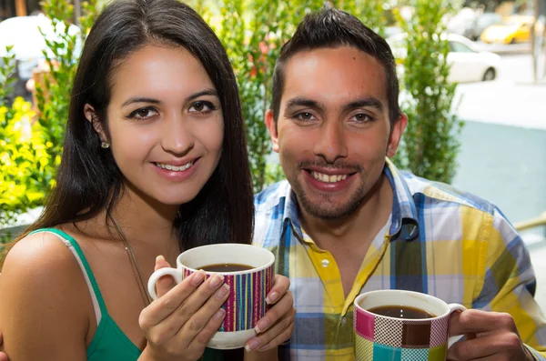 Hispanic cute couple enjoying coffee during a cozy date outdoors and green vegetation background — Stock fotografie