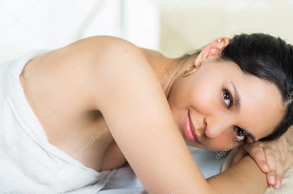 Hispanic brunette model getting massage spa treatment, white towel covering upper body lying horizontal smiling to camera