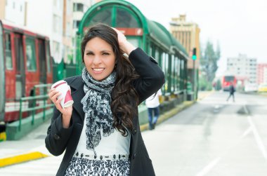 Zarif kadın giyiyor koyu ceket ve siyah giyim kentsel çevre ile arka kameraya gülümseyen duvara karşı ayakta beyaz