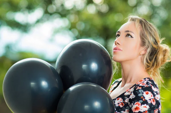 Beautiful hispanic model wearing summer dress posing for camera with black balloons, profile angle — Stock Photo, Image