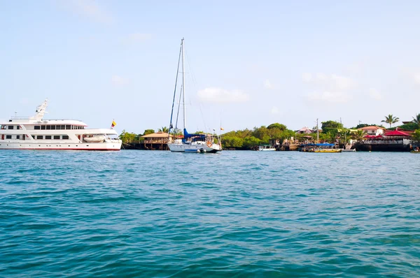 Piccola nave turistica situata all'interno di una tranquilla baia oceanica con barca a vela ancorata accanto, bellissimi dintorni, alcuni edifici sullo sfondo — Foto Stock