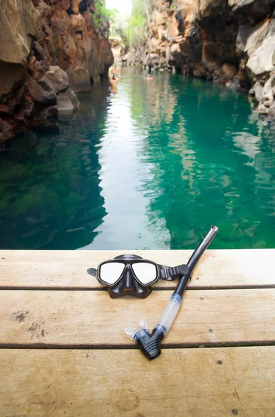 Máscara de mergulho e snorkel deitado no cais de madeira com bela água do oceano verde rodeado por penhascos espetaculares de rocha de ambos os lados, Ilhas Galápagos Equador — Fotografia de Stock