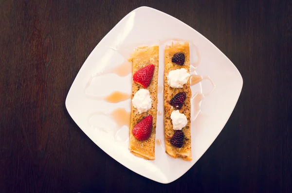 Two beautiful crepes pancakes lying on white plate, decorated with small amount of cream and berries, elegant presentation — Stok fotoğraf
