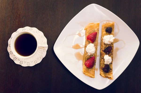 Two beautiful crepes pancakes lying on white plate, decorated with small amount of cream and berries, coffee cup next to it, elegant presentation — Zdjęcie stockowe
