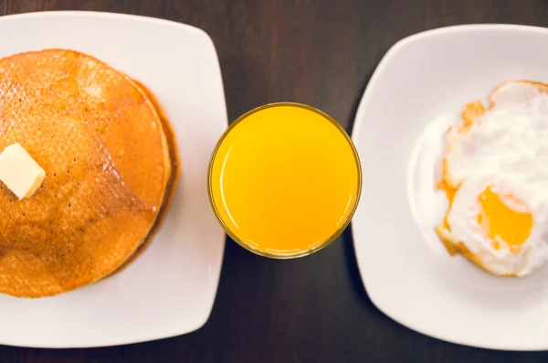 Glas sinaasappelsap met wit platen pannenkoeken en gebakken eieren aan beide zijden, elegante ontbijt concept — Stockfoto
