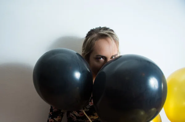 Modelo bonito encostado à parede branca e espreitando a cabeça para fora dos balões — Fotografia de Stock