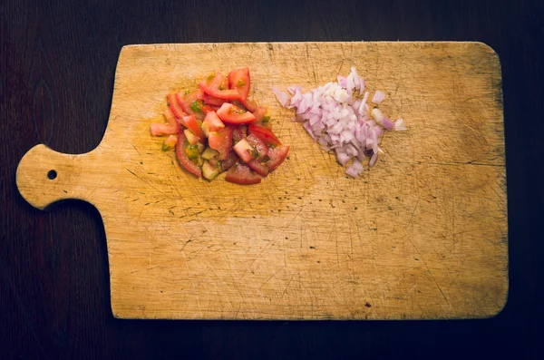 Wooden chopping board with chopped tomatoes and onions, as seen from above — Stock Photo, Image