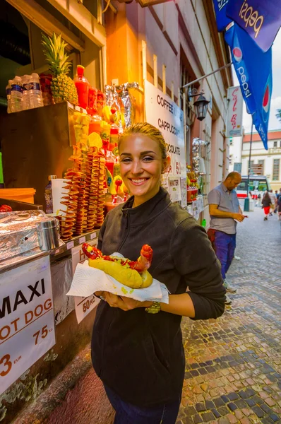 Prague, Czech Republic - 13 August, 2015: Pretty blonde local girl holding up a giant bratwurst sausage in bread and smiling to camera