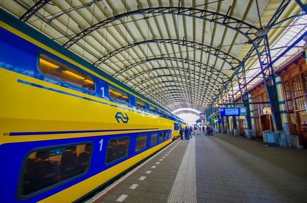 Harlem, Amsterdam, Netherlands - July 14, 2015: Inside railroad station, large roof covering platform, blue and yellow train pulling up