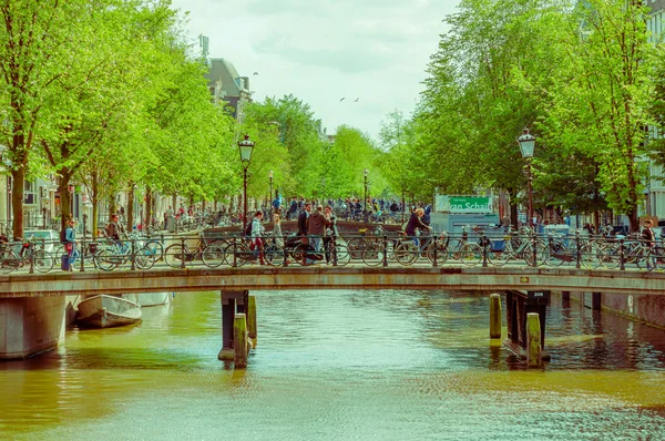 Amsterdam, Pays-Bas - 10 juillet 2015 : Deux ponts s'étendent sur le canal d'eau et des hordes de personnes traversent, la vie quotidienne dans la ville — Photo