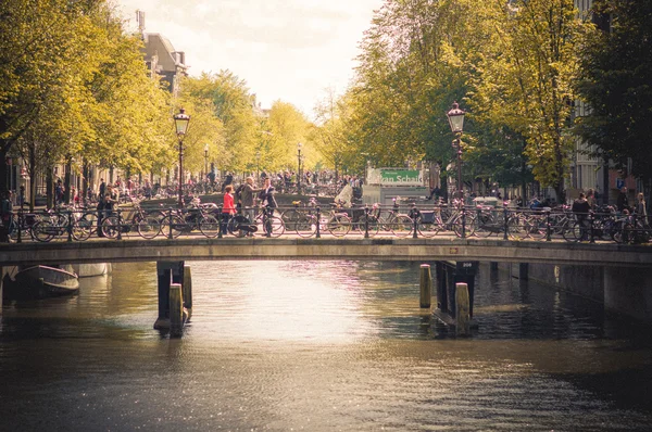 Ámsterdam, Países Bajos - 10 de julio de 2015: Dos puentes se extienden sobre el canal de agua y hordas de personas cruzando, la vida cotidiana en la ciudad —  Fotos de Stock