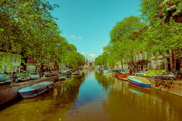 Amsterdam, Niederlande - 10. Juli 2015: Wasserkanal von einer kleinen Brücke aus gesehen, grüne Bäume und Wohngebäude entlang — Stockfoto