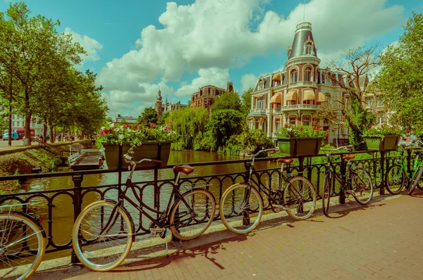 Amszterdam, Hollandia - 2015. július 10.: Ül a vízparton, gyönyörű épület homlokzati kerékpárok parkolt a híd előtt — Stock Fotó