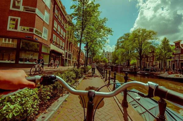 Amszterdam, Hollandia - 2015. július 10.: Motorosok szempontból biciklis város utcáin, a gyönyörű sumer nap-, víz-csatorna jobb oldalán — Stock Fotó