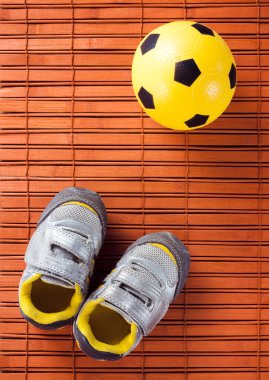 Çocuk spor ayakkabı ve futbol topu bir ahşap zemin üzerinde. Üstten Görünüm