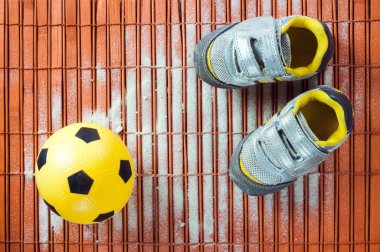 Çocuk spor ayakkabı ve futbol topu bir ahşap zemin üzerinde. Üstten Görünüm