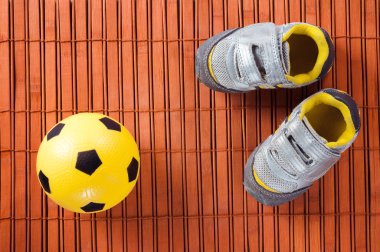 Çocuk spor ayakkabı ve futbol topu bir ahşap zemin üzerinde. Üstten Görünüm