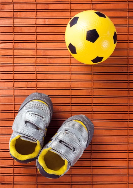 Çocuk spor ayakkabı ve futbol topu bir ahşap zemin üzerinde. Üstten Görünüm