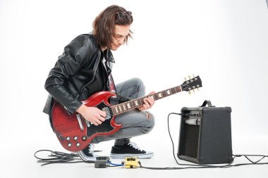 Focused handsome young guitarist playing electric guitar with amplifier