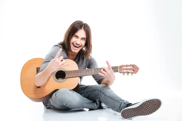 Lächelnder Mann mit Gitarre sitzt und macht Rock-Geste — Stockfoto