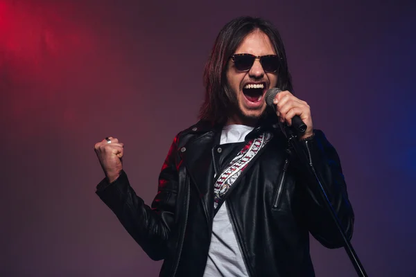 Atractivo joven cantante masculino con el canto de pelo largo usando micrófono —  Fotos de Stock