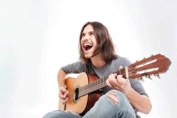 Счастливый молодой человек с длинными волосами играет на гитаре и поет — стоковое фото