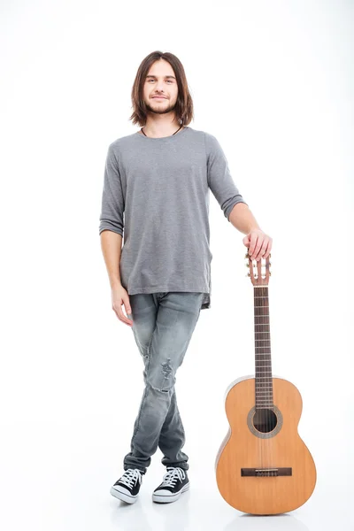 Smiling attractive young man standing and holding guitar — Stock Photo, Image