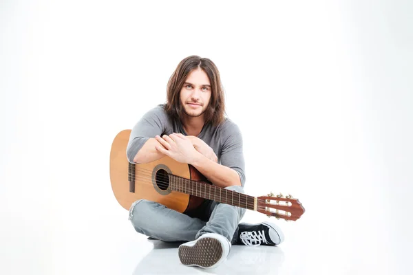 Привлекательный молодой человек с длинными волосами сидит и держит гитару — стоковое фото