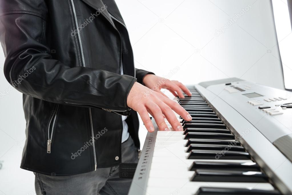 Hands of young man standing and playing on synthesizer