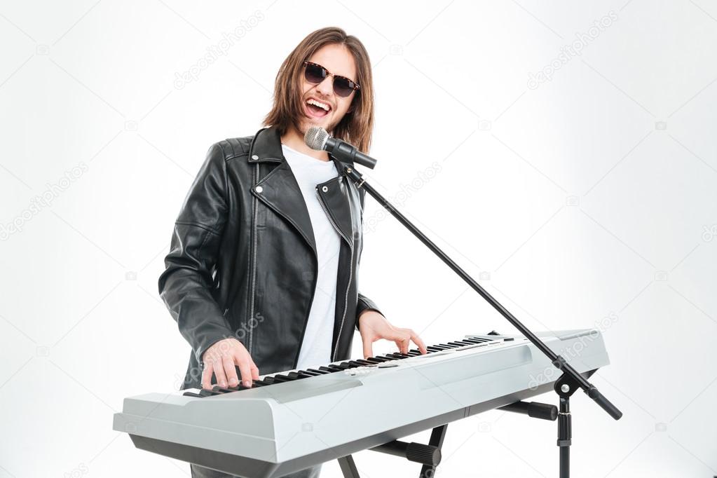 Happy attractive man singing in microphone and playing on synthesizer