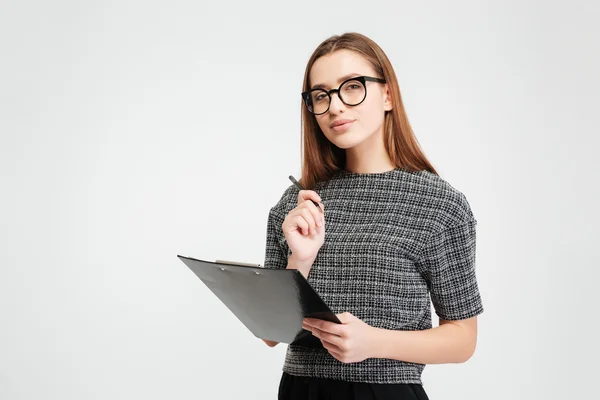 Mujer joven pensativa en gafas sujetando portapapeles y bolígrafo — Foto de Stock