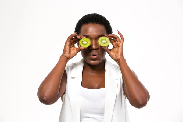 Funny  african woman holding kiwi halves in front of eyes — Stock Fotó