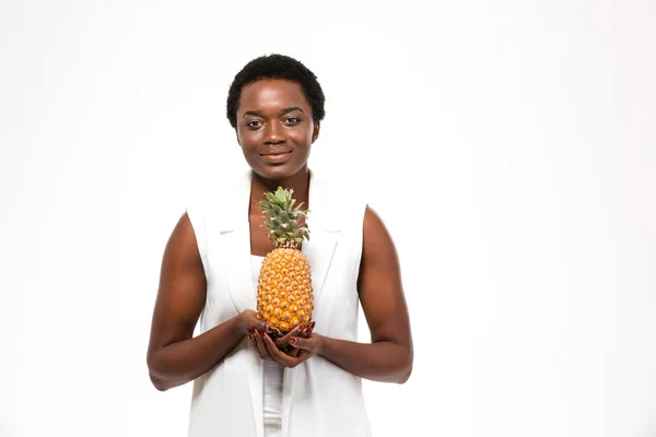 Smiling pretty african american young woman standing and holding pineapple — стокове фото