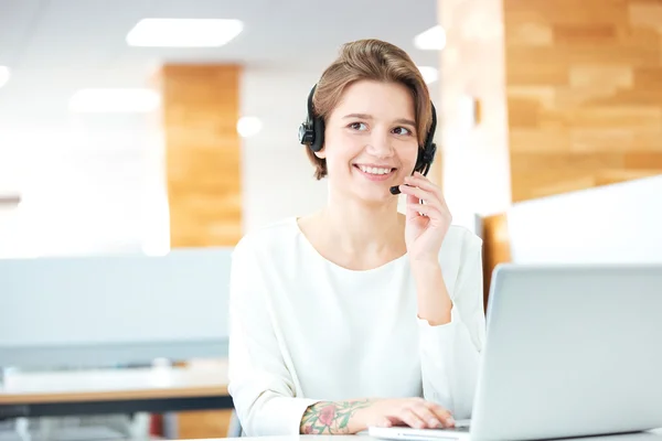 Joven atractiva alegre que trabaja con auriculares y portátil — Foto de Stock