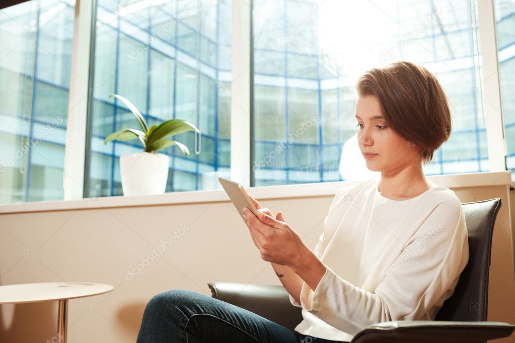 Pensive woman sitting in office and using tablet