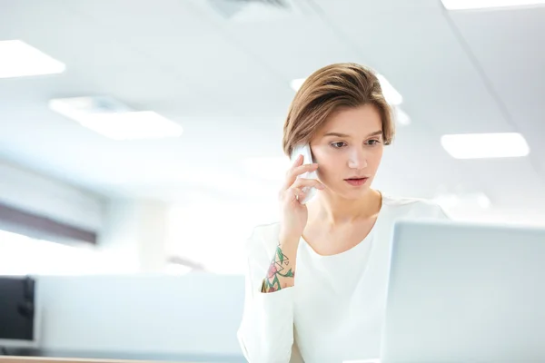 Mujer joven y pensativa hablando por teléfono celular en la oficina — Foto de Stock