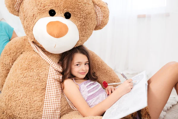 Menina sorridente bonito deitado em grande urso de pelúcia e desenho — Fotografia de Stock