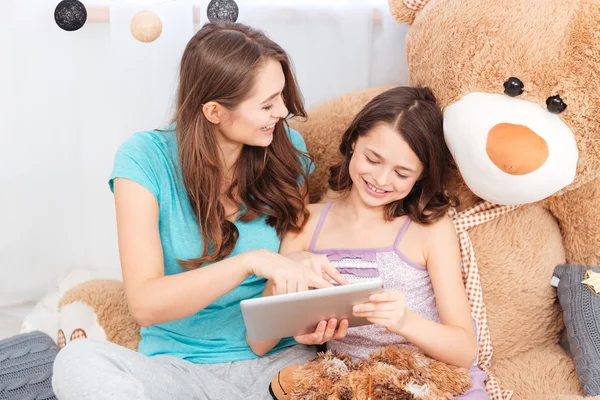 Two cheerful cute sisters sitting and using tablet together — Stock Photo, Image