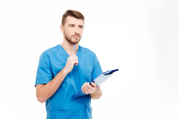 Pensive male doctor standing with clipboard — Stock Photo, Image