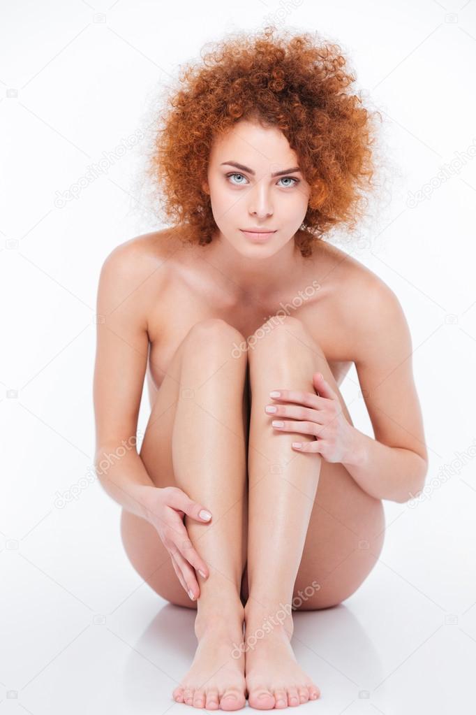 Naked woman with curly hair sitting on the floor