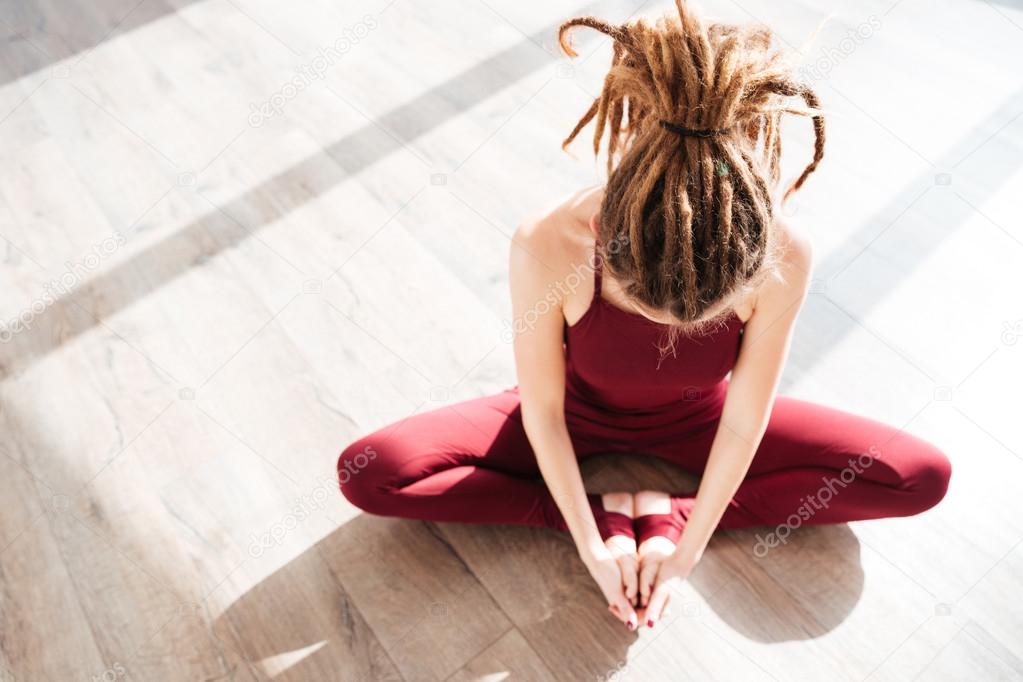 Modern young woman with dreadlocks sitting and doing yoga
