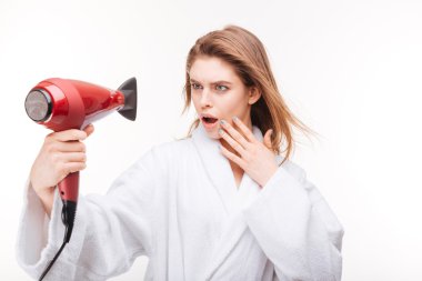 Şaşırmış güzel genç kadın saç kurutma ve kurutucu içine bakarak 