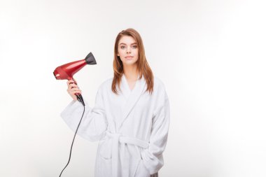 Attractive young woman in bathrobe standing and holding hair dryer