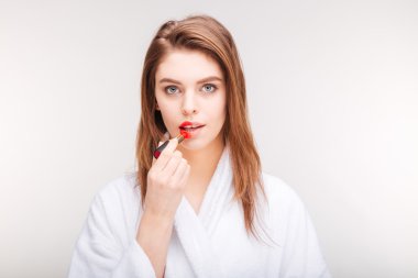 Beautiful sensual woman trying red lipstick on half of lips