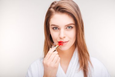 Pretty smiling young woman using lipstick on half of lips